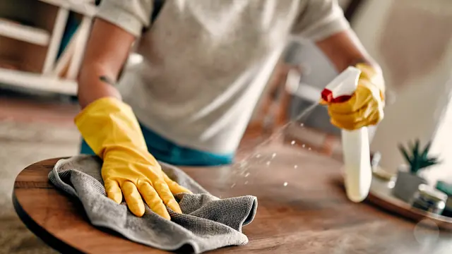 Tisch wird mit Mikrofasertuch und Spray gereinigt